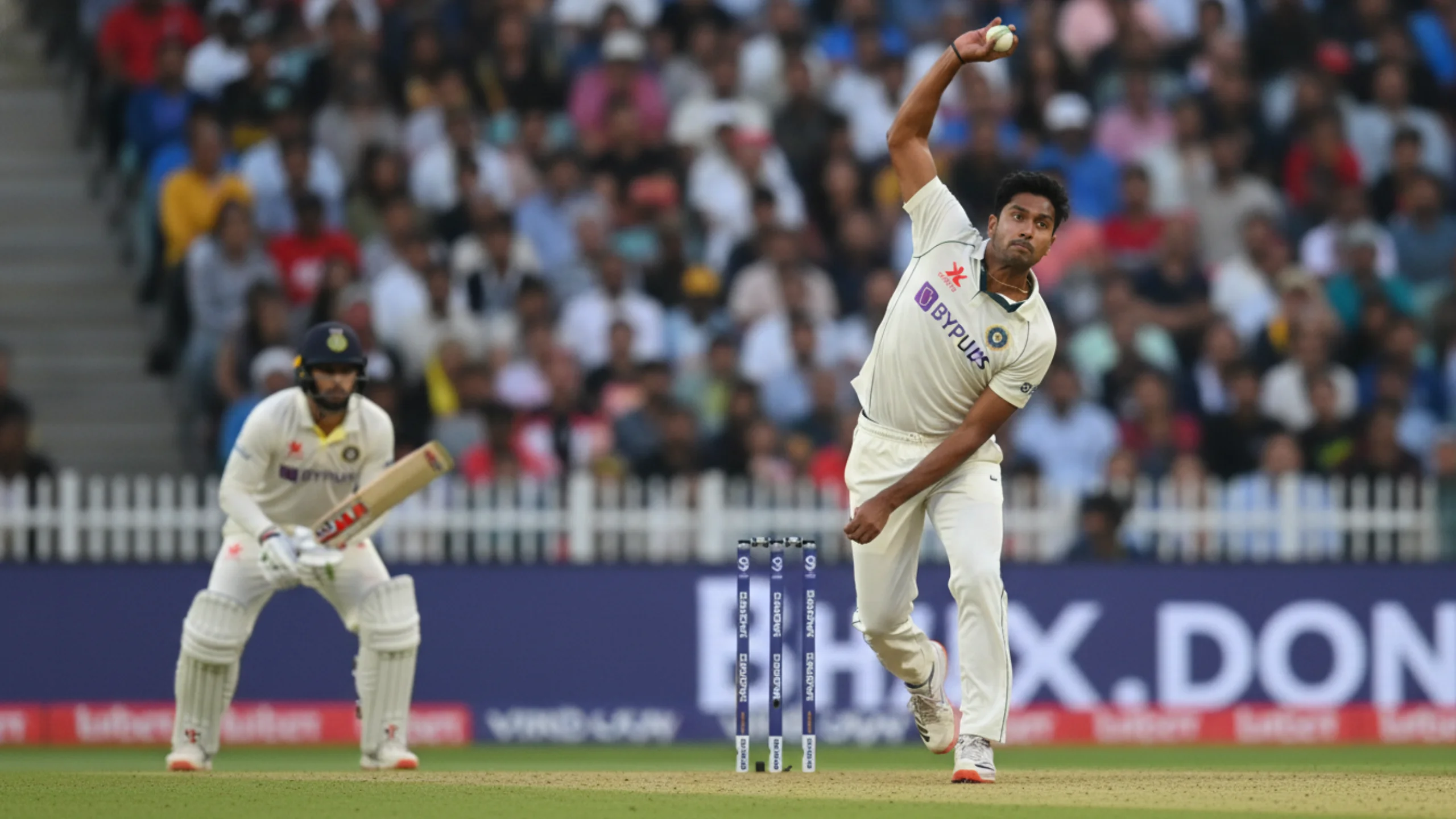Dynamic action shot of a cricket bowler in mid-delivery stride with batsman ready in the background, capturing the intensity of live match action